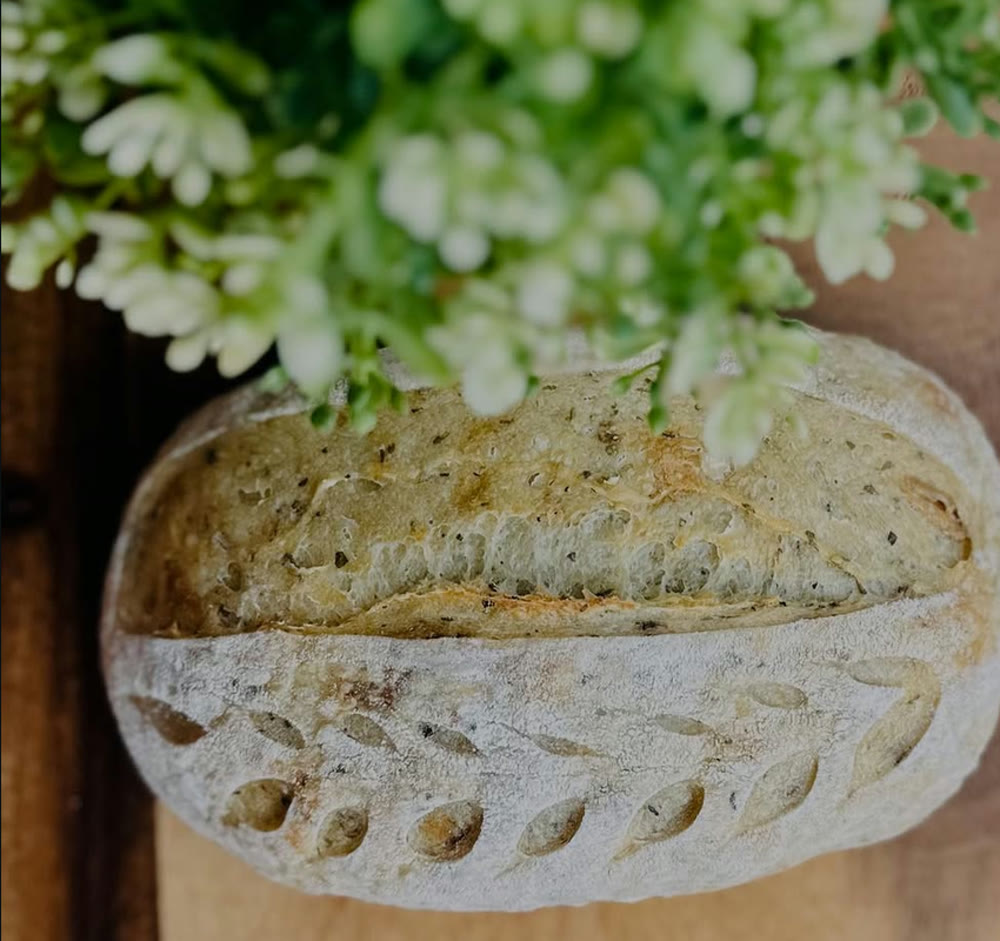A scored herb sourdough loaf on a wooden board
